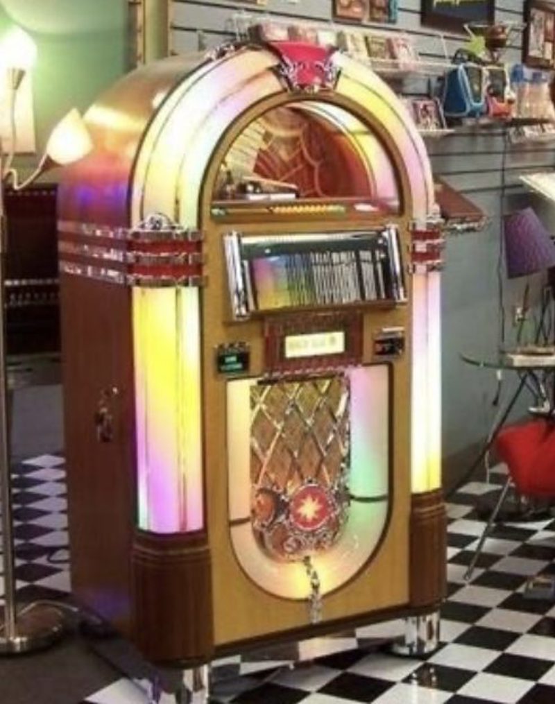 A Wurlitzer 1015 “Bubbler” jukebox lit up on a black-and-white tiled diner floor