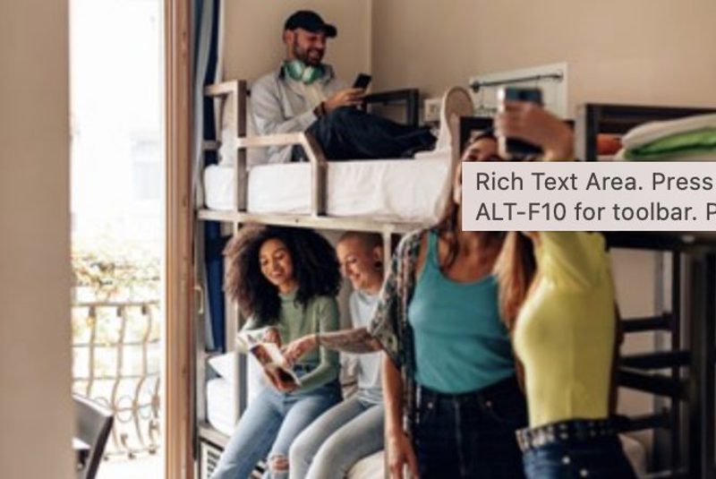Young travellers talking and taking photographs in a hostel dormitory furnished with bunk beds