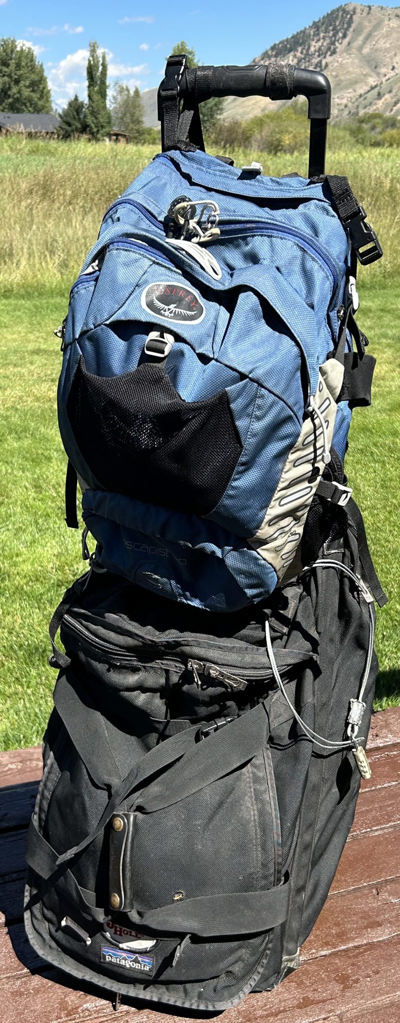 Scott's blue Osprey daypack strapped on top of his black Patagonia rolling bag, the compartments secured with an airline cable and lock