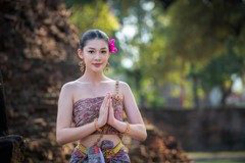 A Thai woman in traditional dress offering the ‘wai’ greeting, palms pressed together at her chest