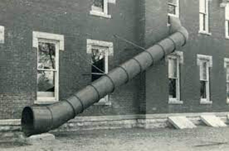 A spiral metal fire-escape chute running from an upper window down the side of an old brick building