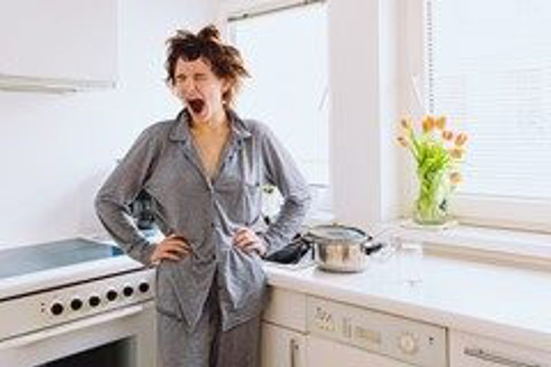 A woman in pyjamas standing in a kitchen, yelling in exasperation