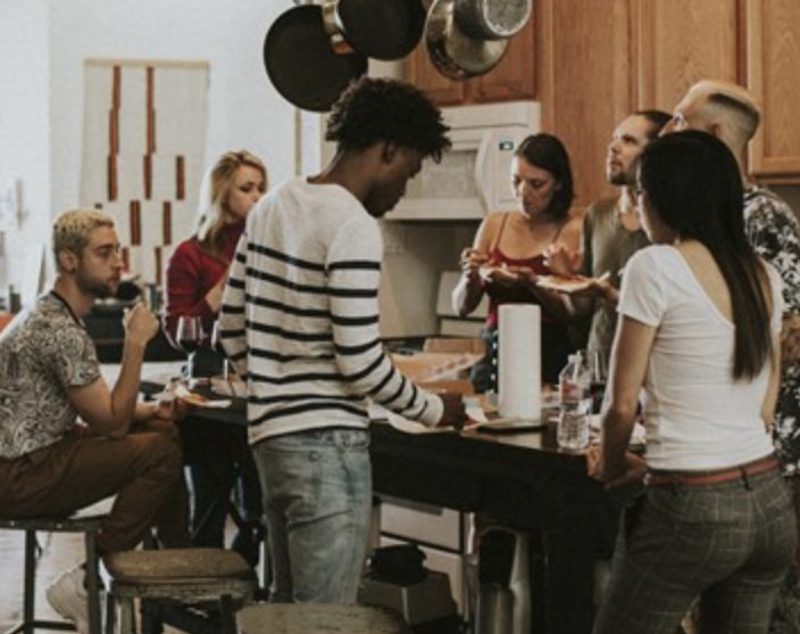 Travellers cooking and eating together around the counter of a shared hostel kitchen